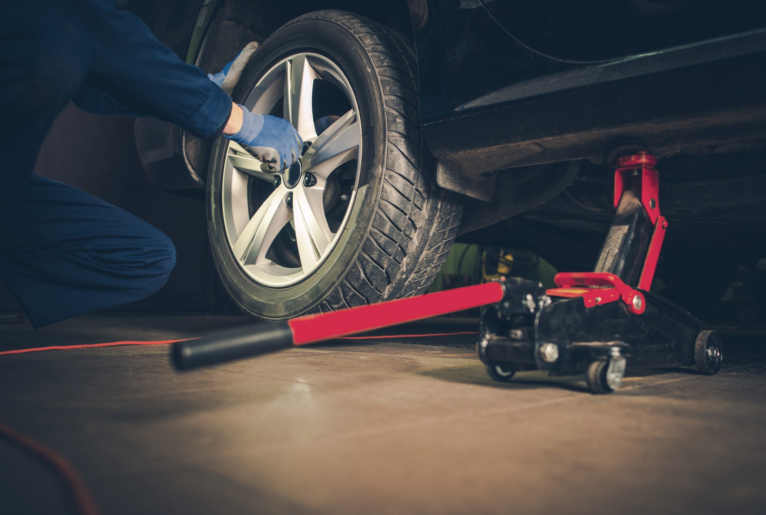 A mechanic using a jack to lift a car while removing a wheel.